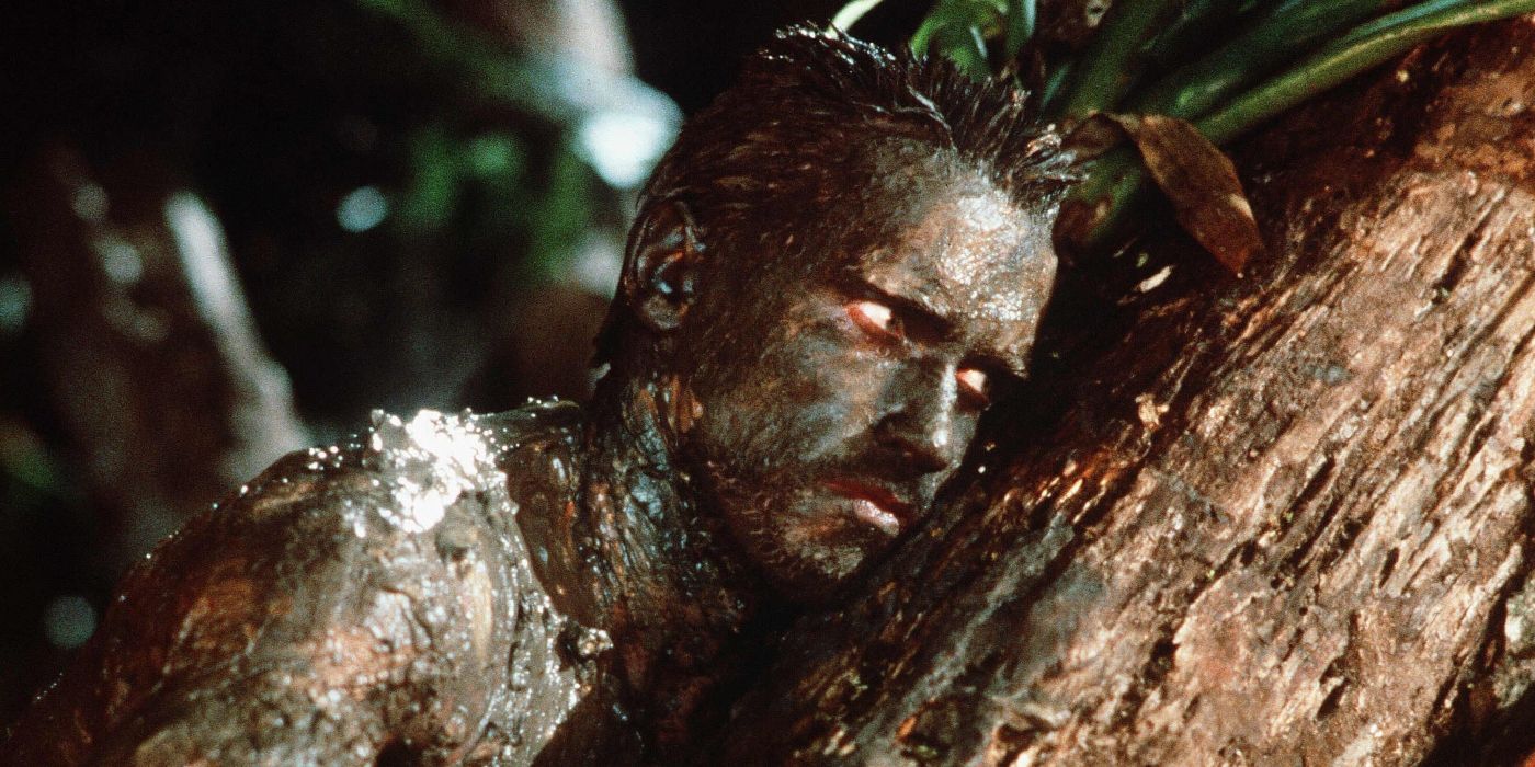 Arnold Schwarzenegger covered in mud and leaning on a tree trunk in Predator