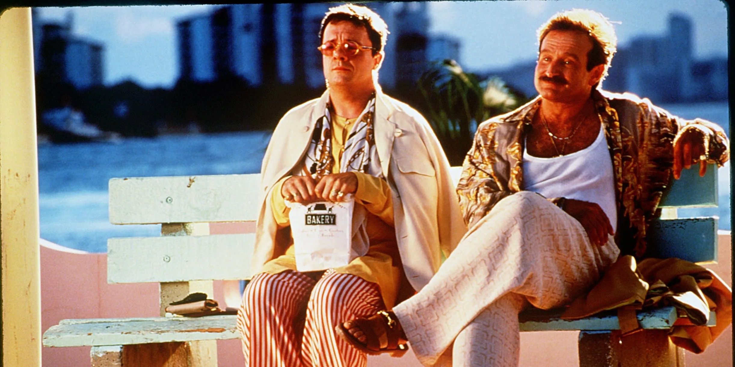 Albert and Armand sitting together on a bench and looking ahead in The Birdcage.
